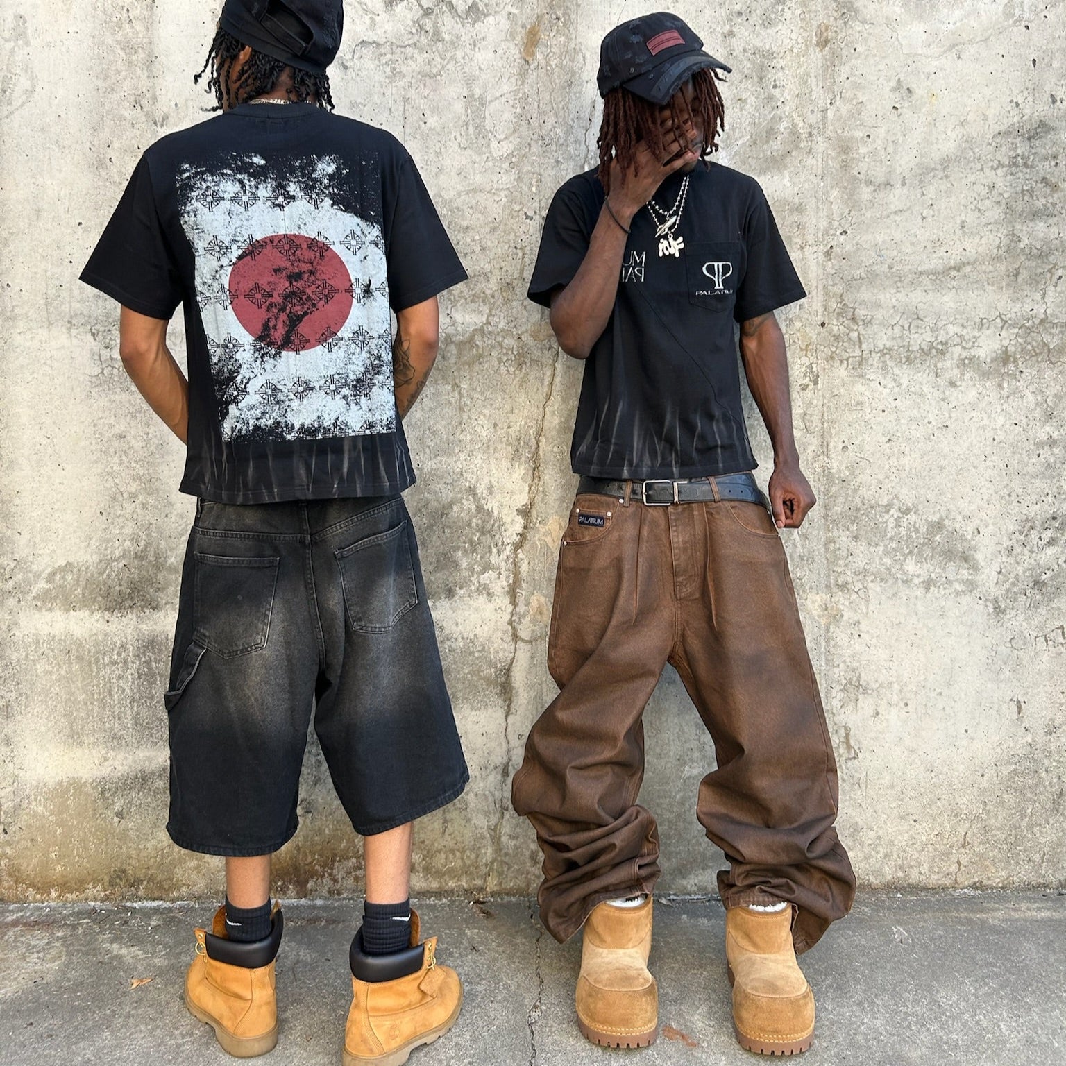 Two people wearing black t-shirts with unique designs against a textured wall.